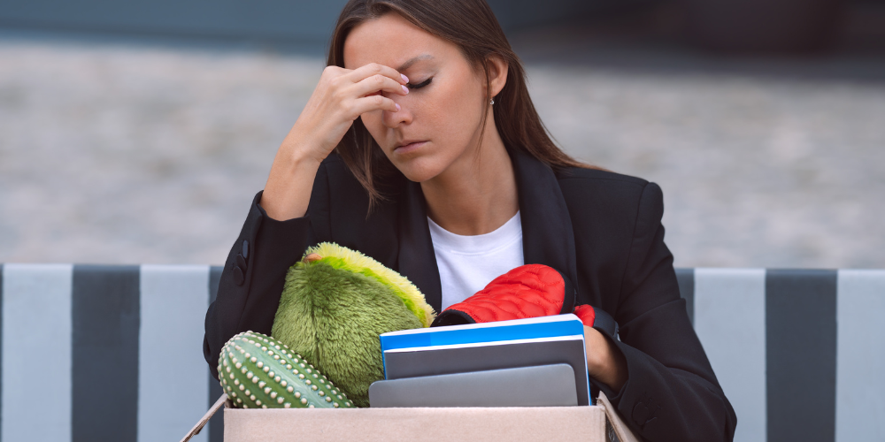 A distressed woman with a box of personal items, possibly after a job loss or office relocation.