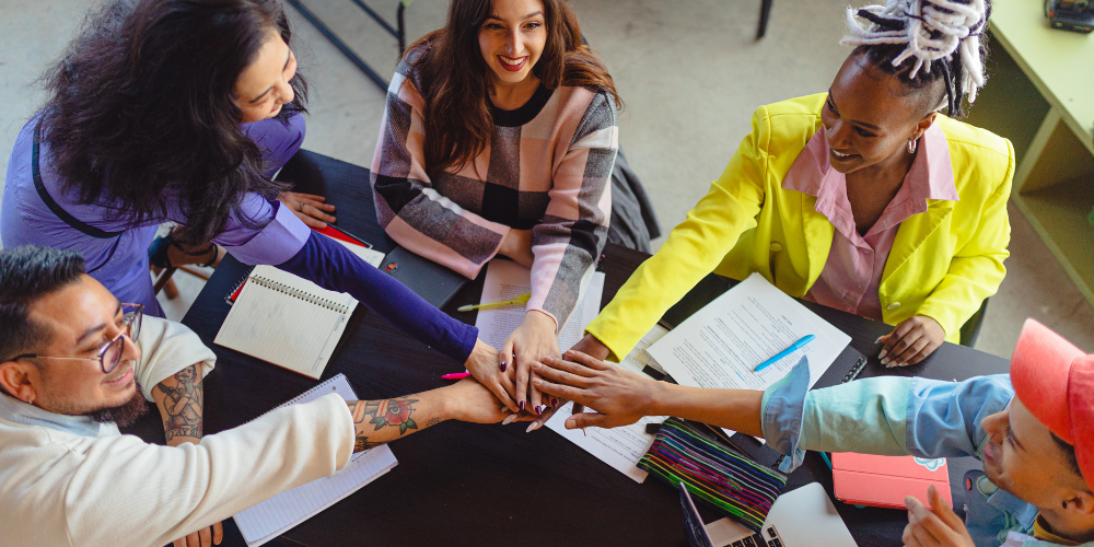 A dynamic overhead view of a diverse team engaging in a teamwork exercise, possibly during a meeting.