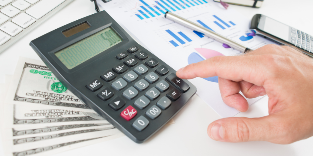A person calculating finances using a calculator, with money and financial documents spread out on the desk.