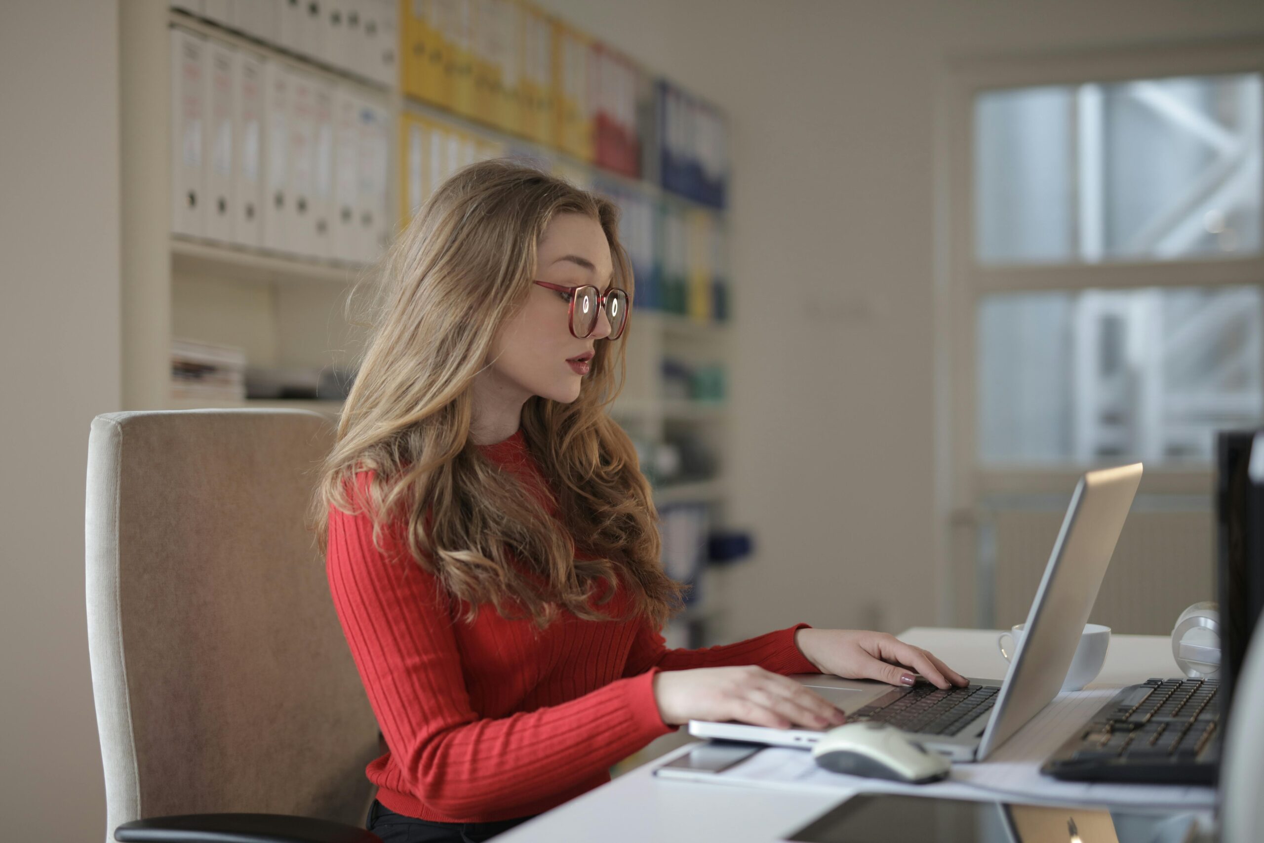 Woman in red sweater working on a laptop, benefiting from outsourced accounting services.