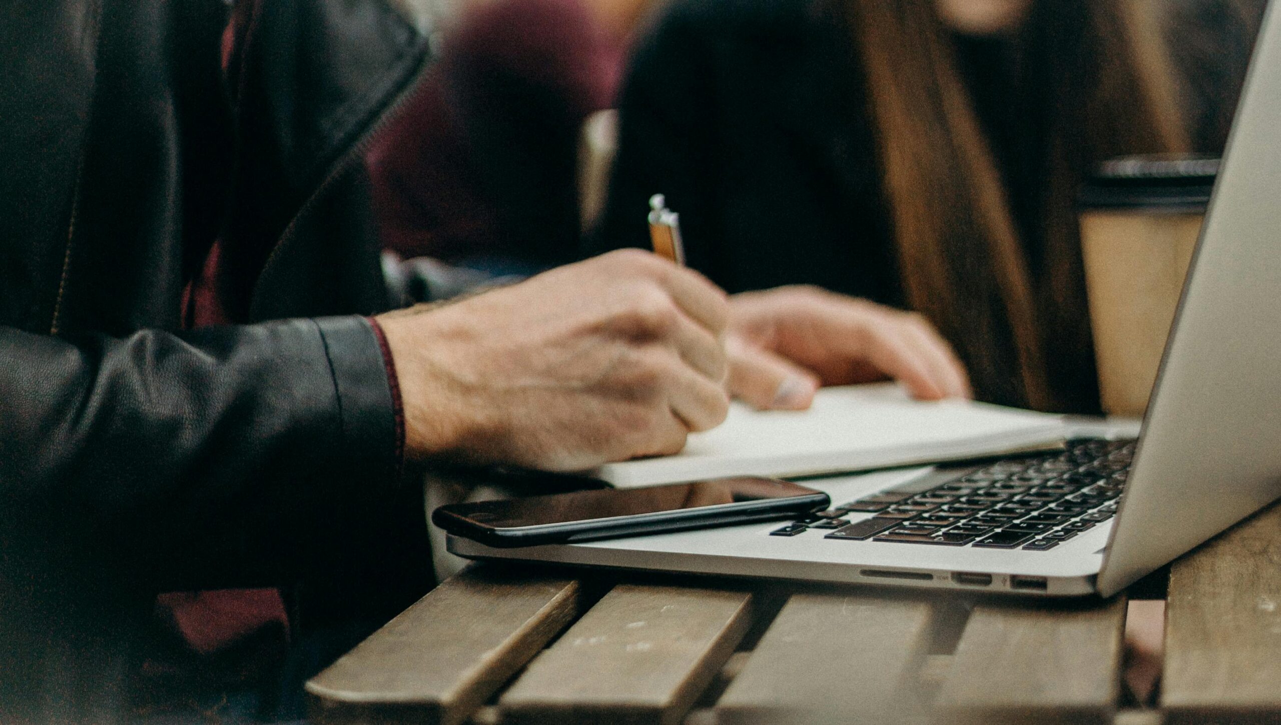 Man writing notes beside his laptop in a café.