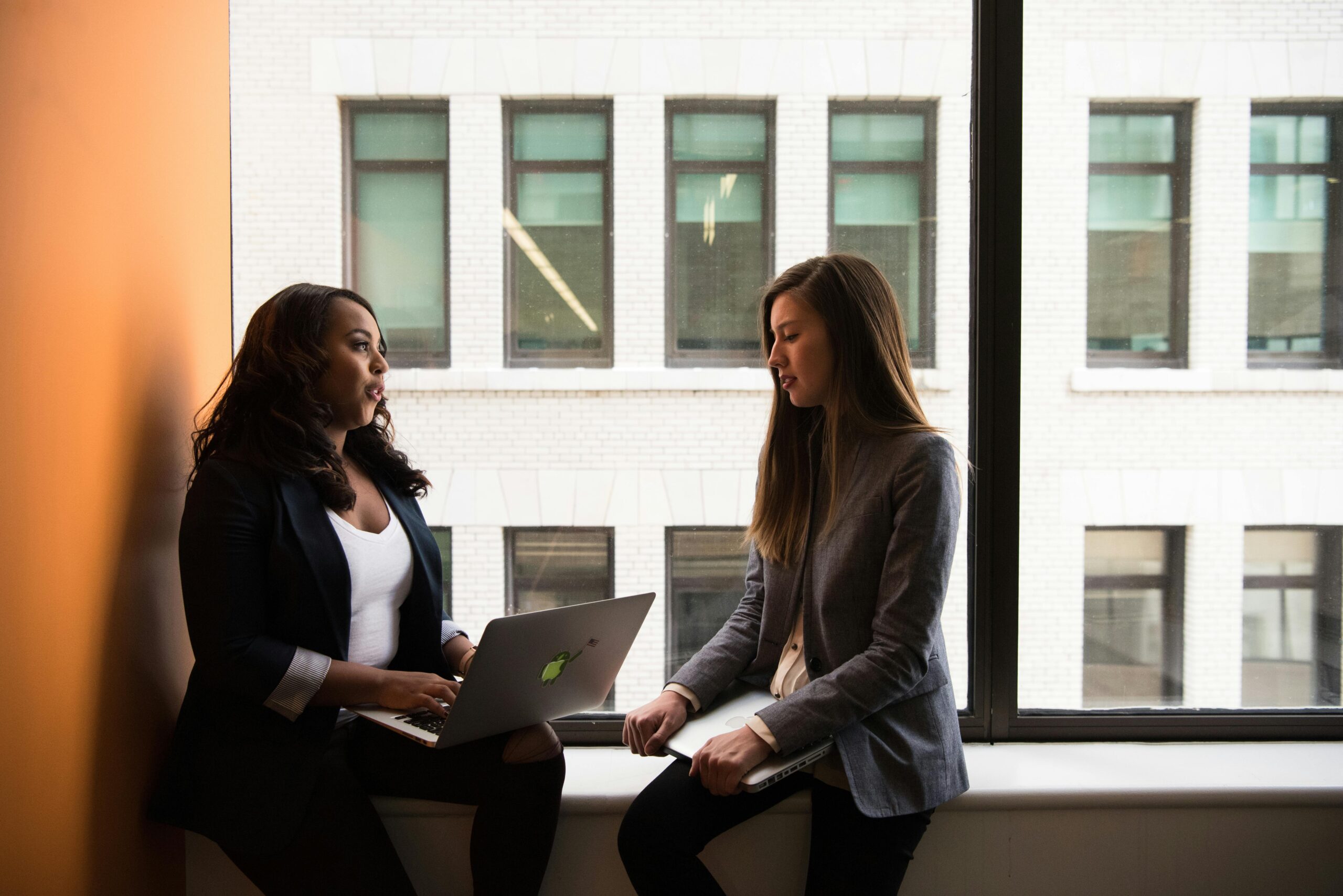 Two professionals discussing what to say in a job interview follow-up email by a window.