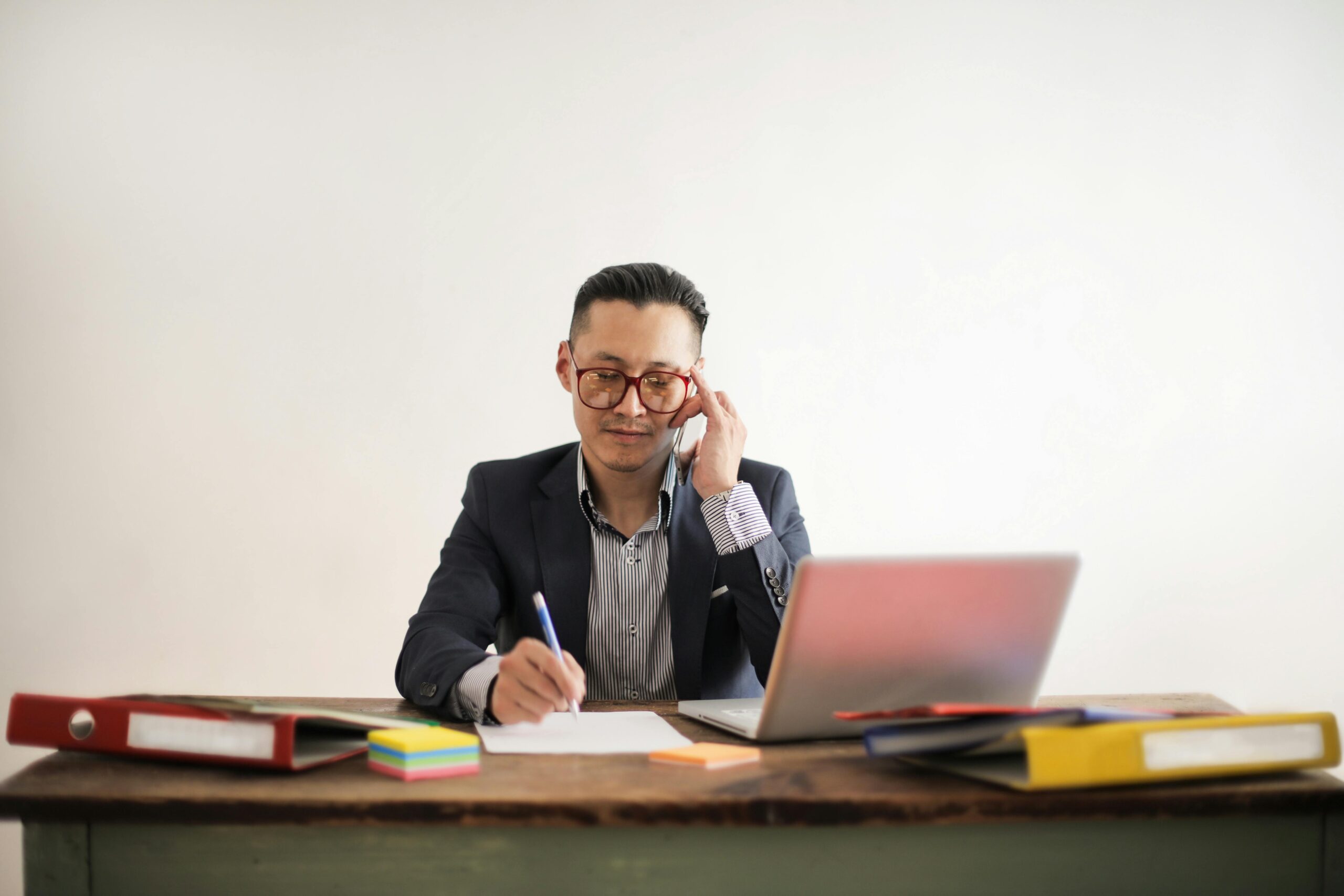 A professional talking on the phone while taking notes, a common scenario in IT assistant jobs.