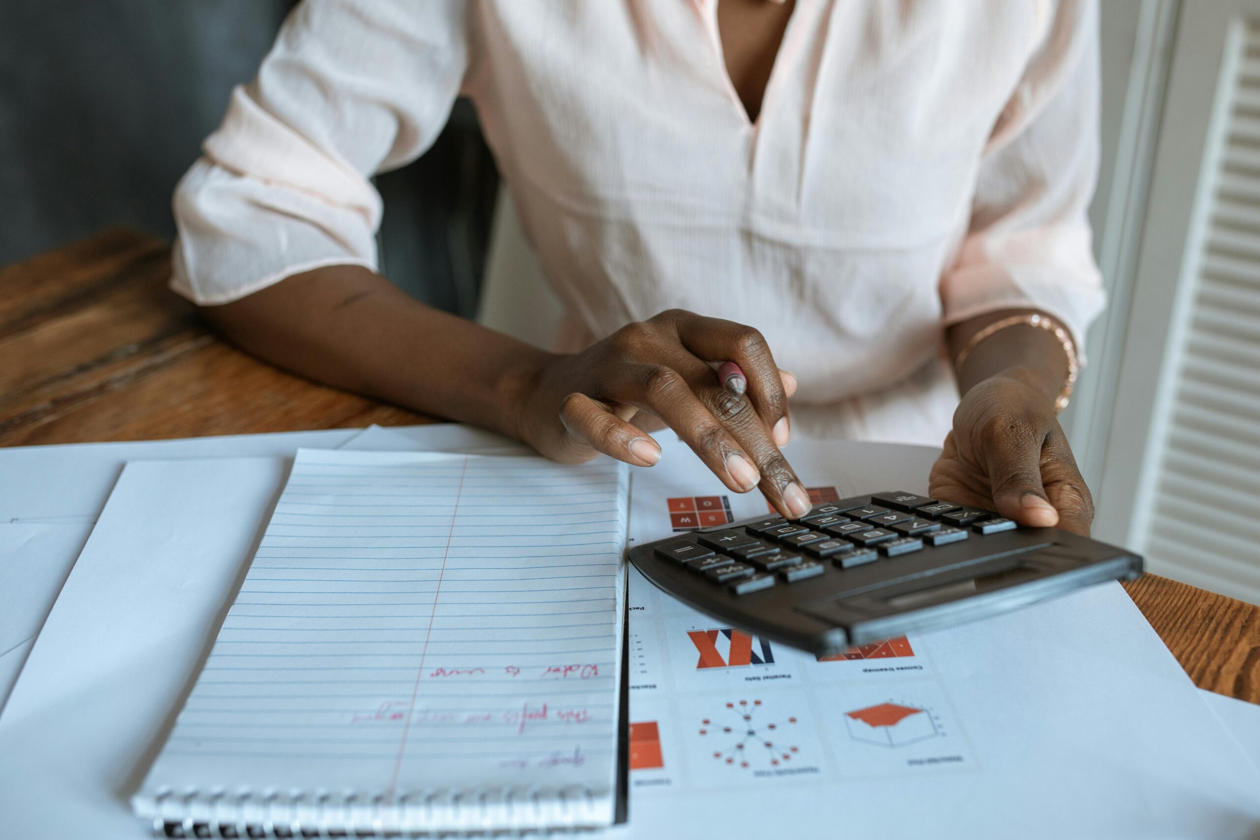 A person using a calculator to analyze financial data, representing outsourced sales analytics.
