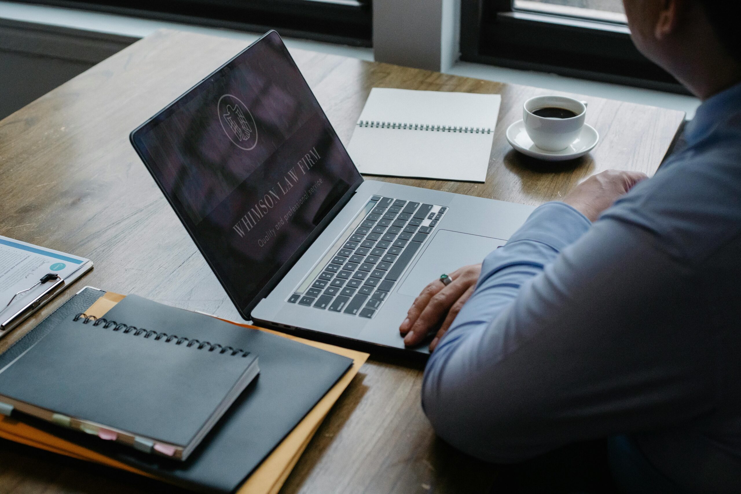 Virtual executive assistant working on a laptop at a desk, surrounded by notebooks and coffee.