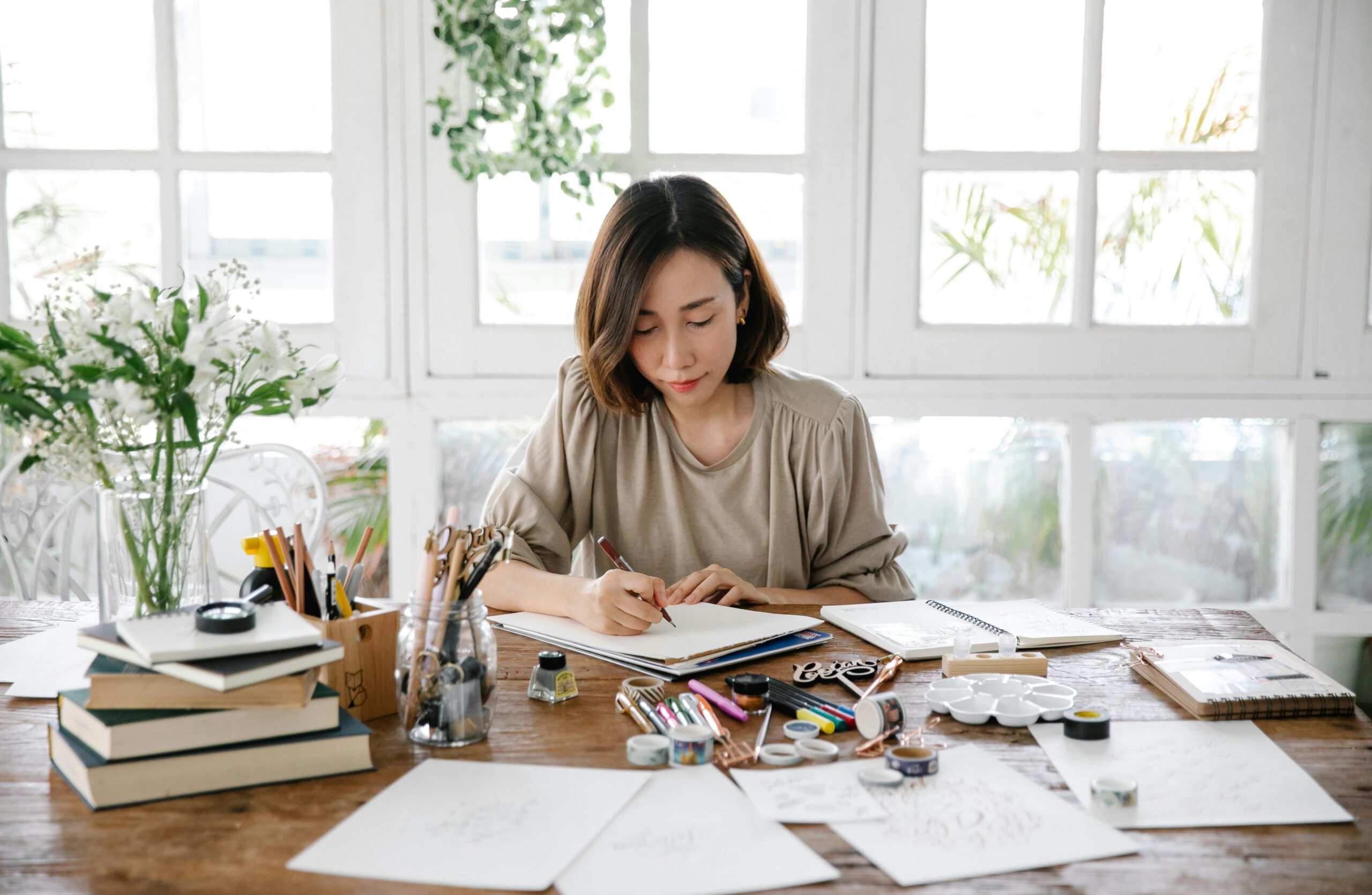 Woman sketching designs at a desk filled with art supplies.