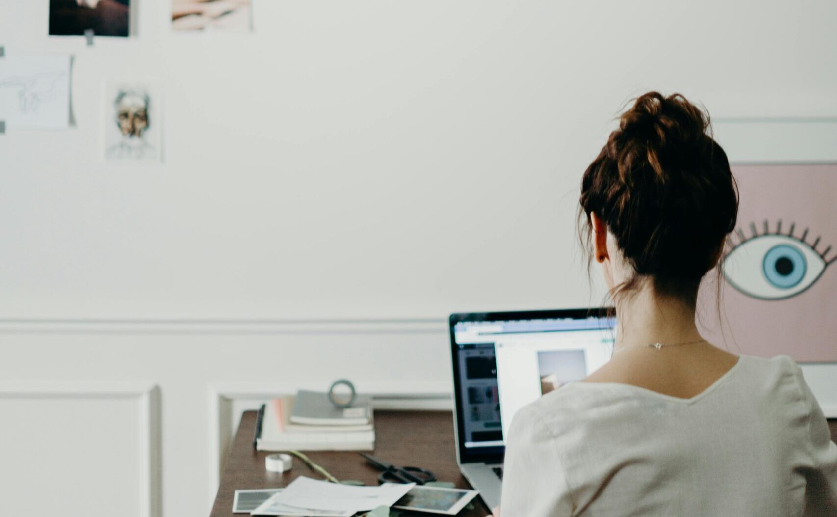 Woman working on a laptop with creative hanging lights. Investigating how much does it cost to hire a designer.