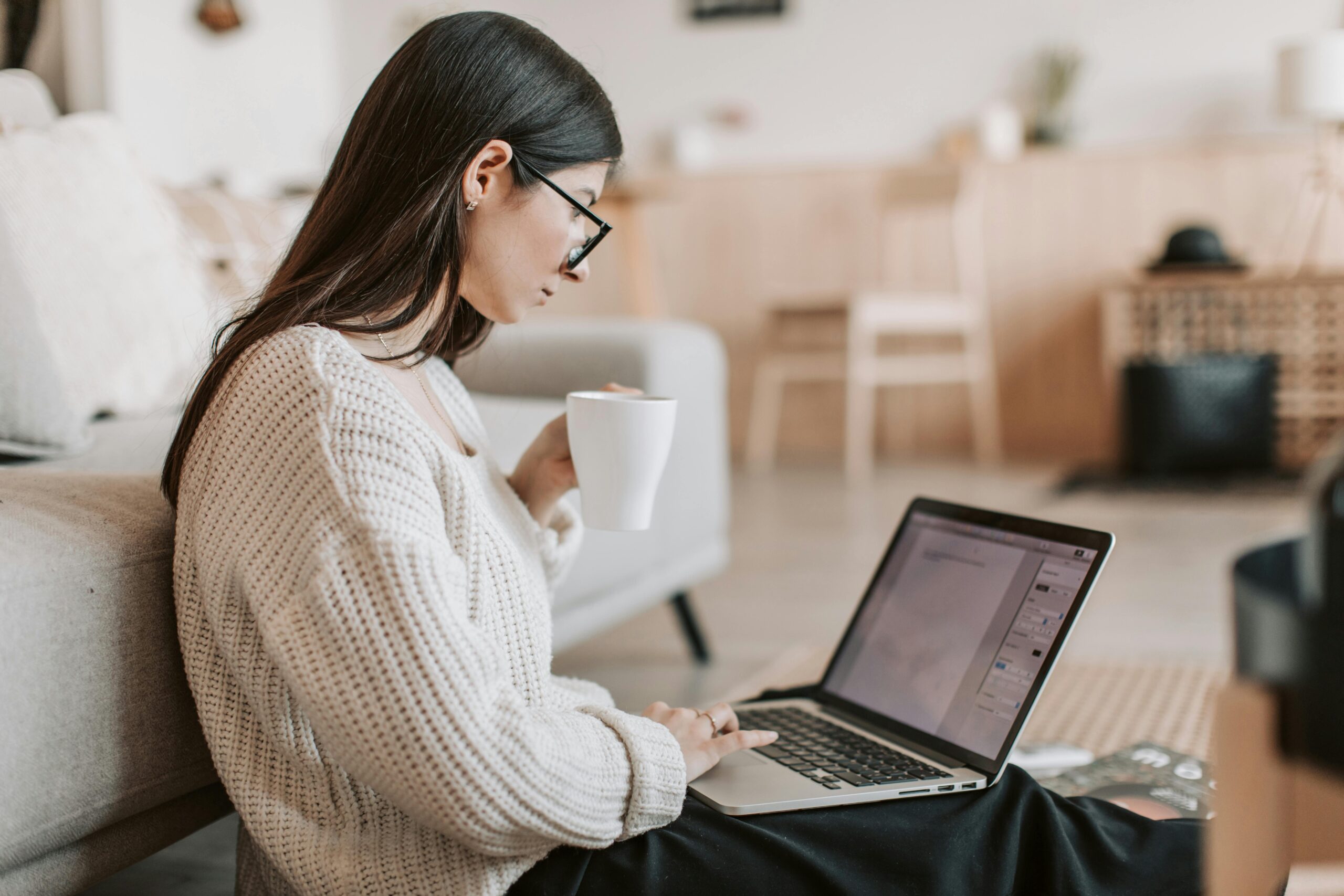 Woman using a laptop while holding a cup.