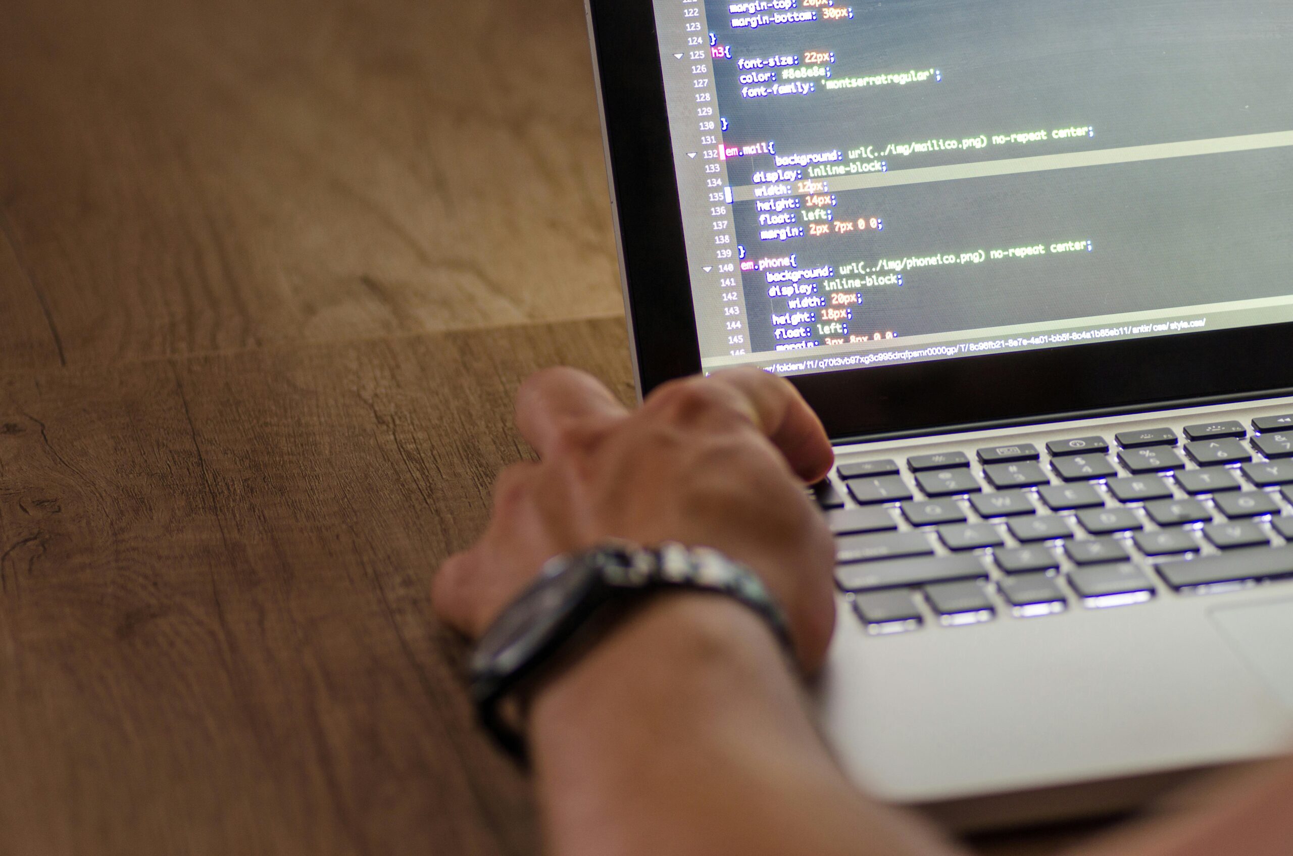 Close-up of hands typing on a laptop with code on the screen. Managing remote developers efficiently.