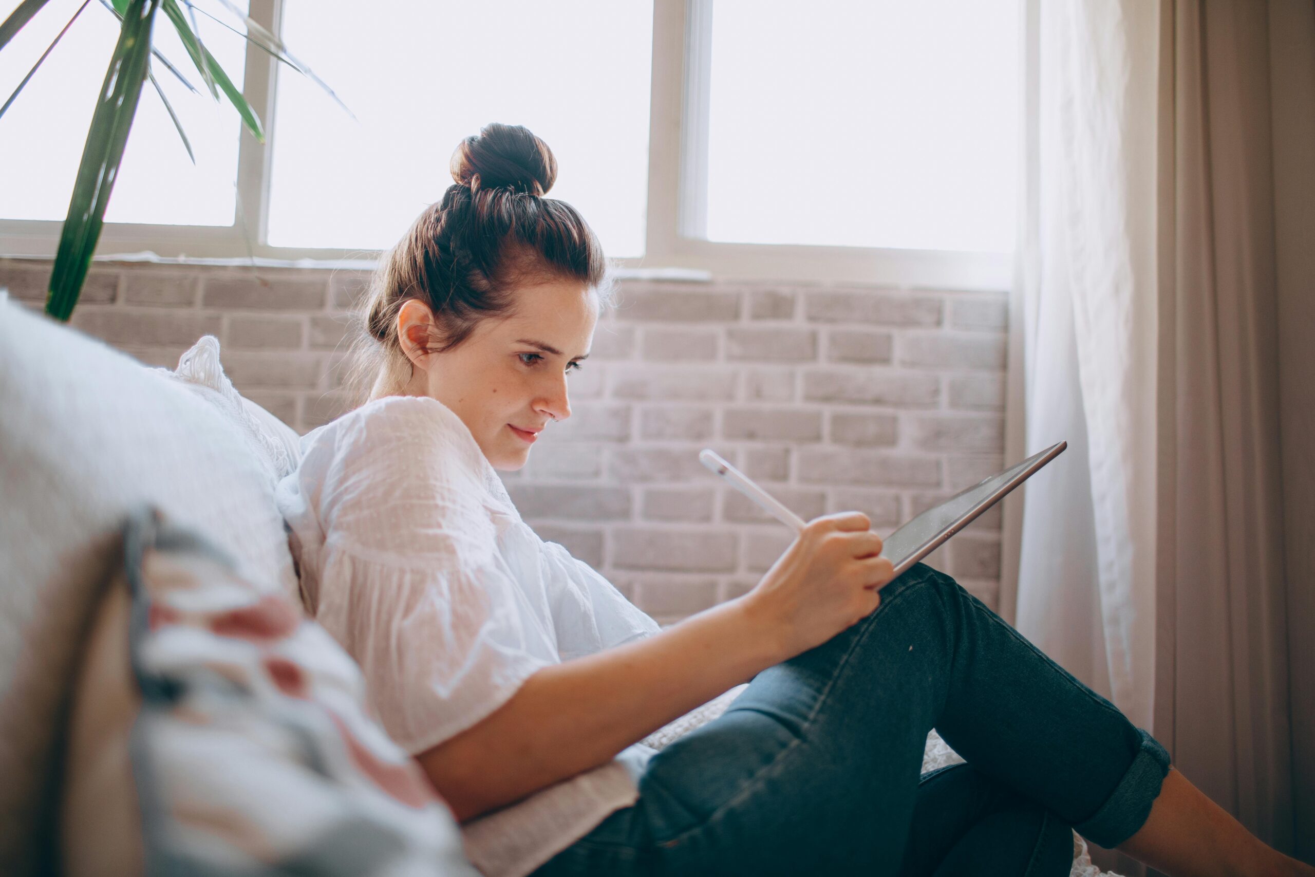 A woman working remotely on a tablet while sitting on a couch, highlighting the flexibility of remote recruiters jobs.