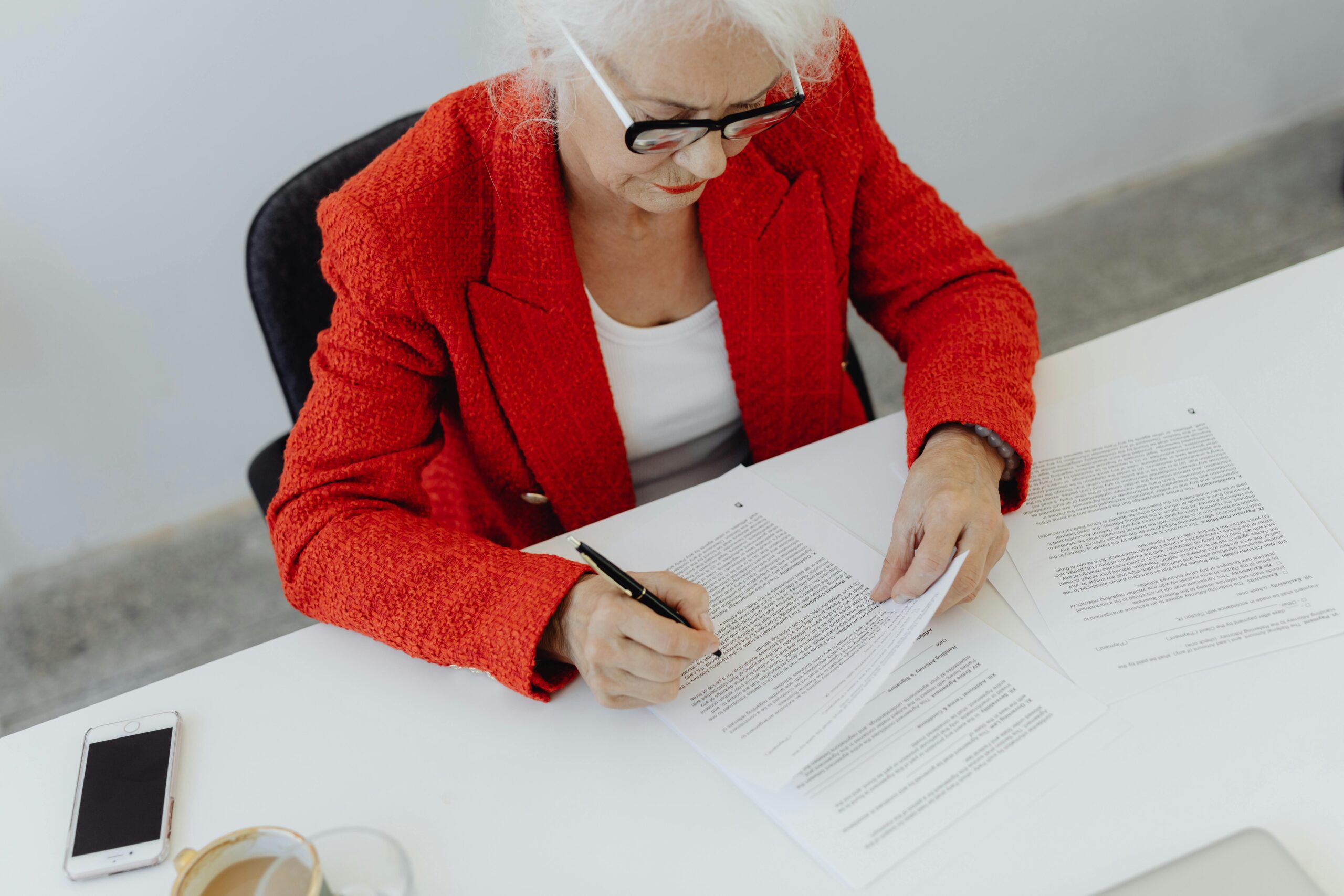 Woman in a red blazer signing papers, showing how to draft a cancelling a contract letter sample.