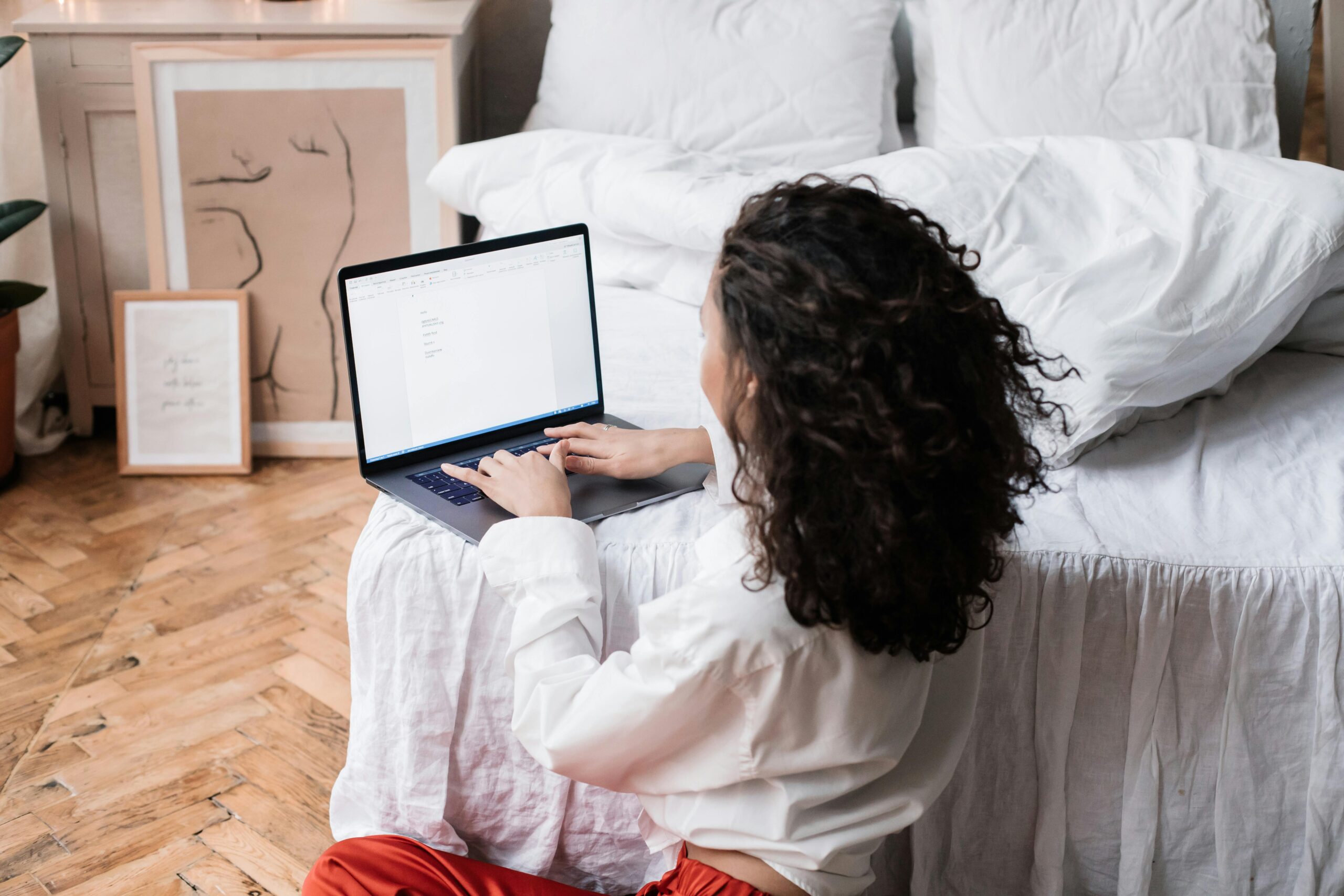Woman working on a laptop from her bed for offshore team management