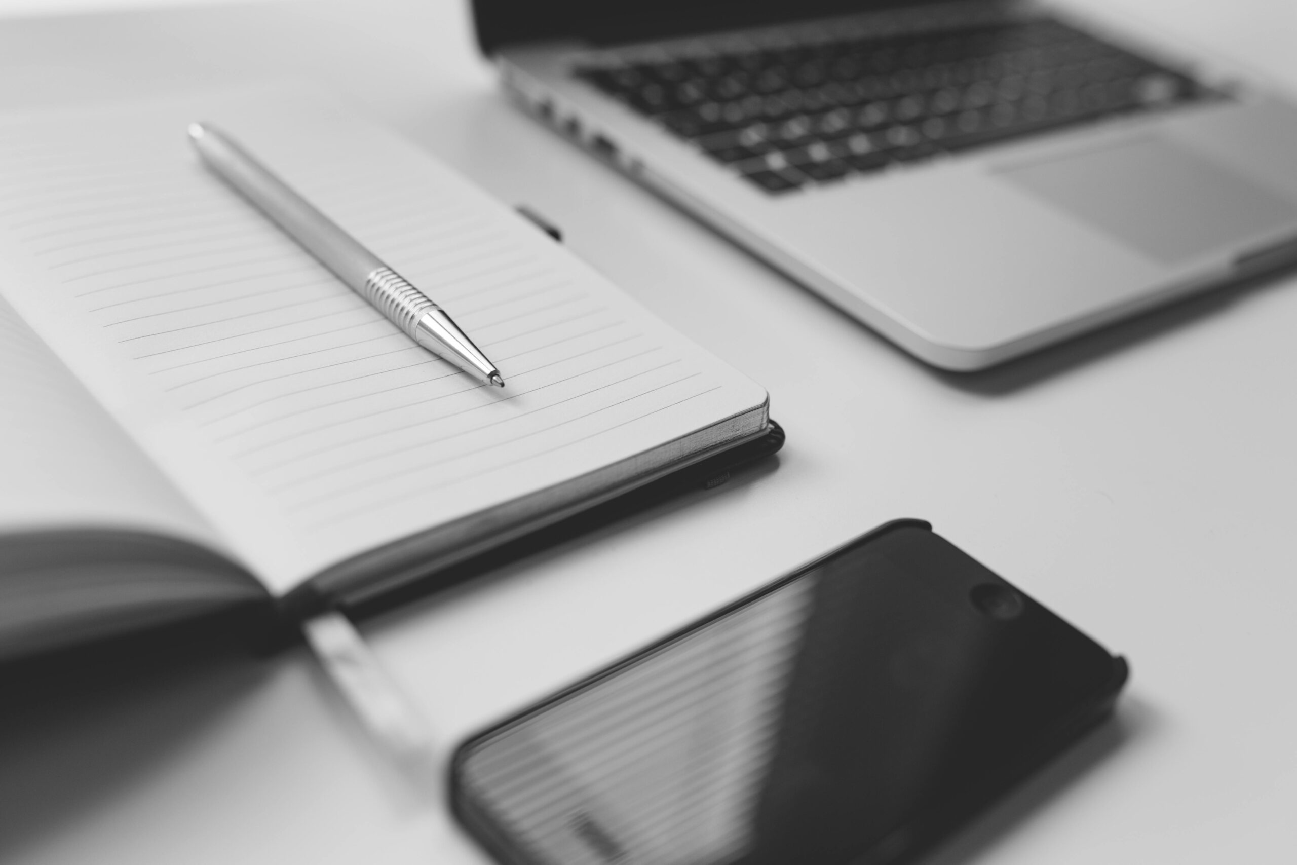 Close-up of a desk with a laptop, notebook, pen, and phone, illustrating tools used by copywriters.
