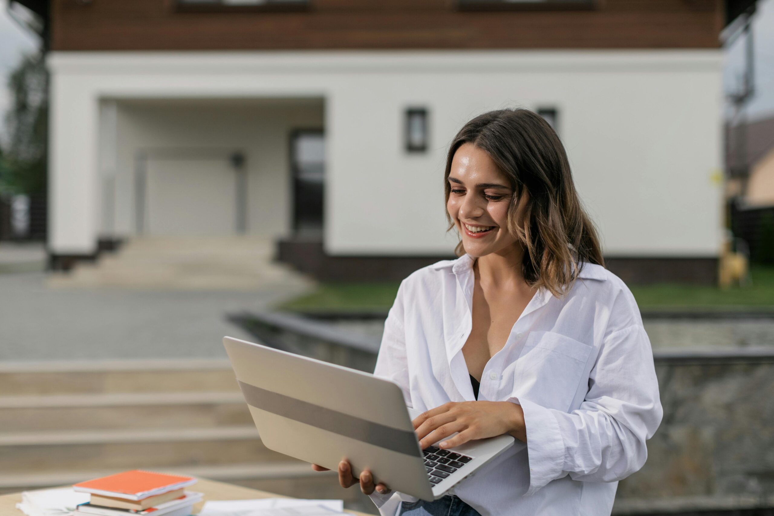 A woman smiling while working on a virtual secretary job description outside a house.