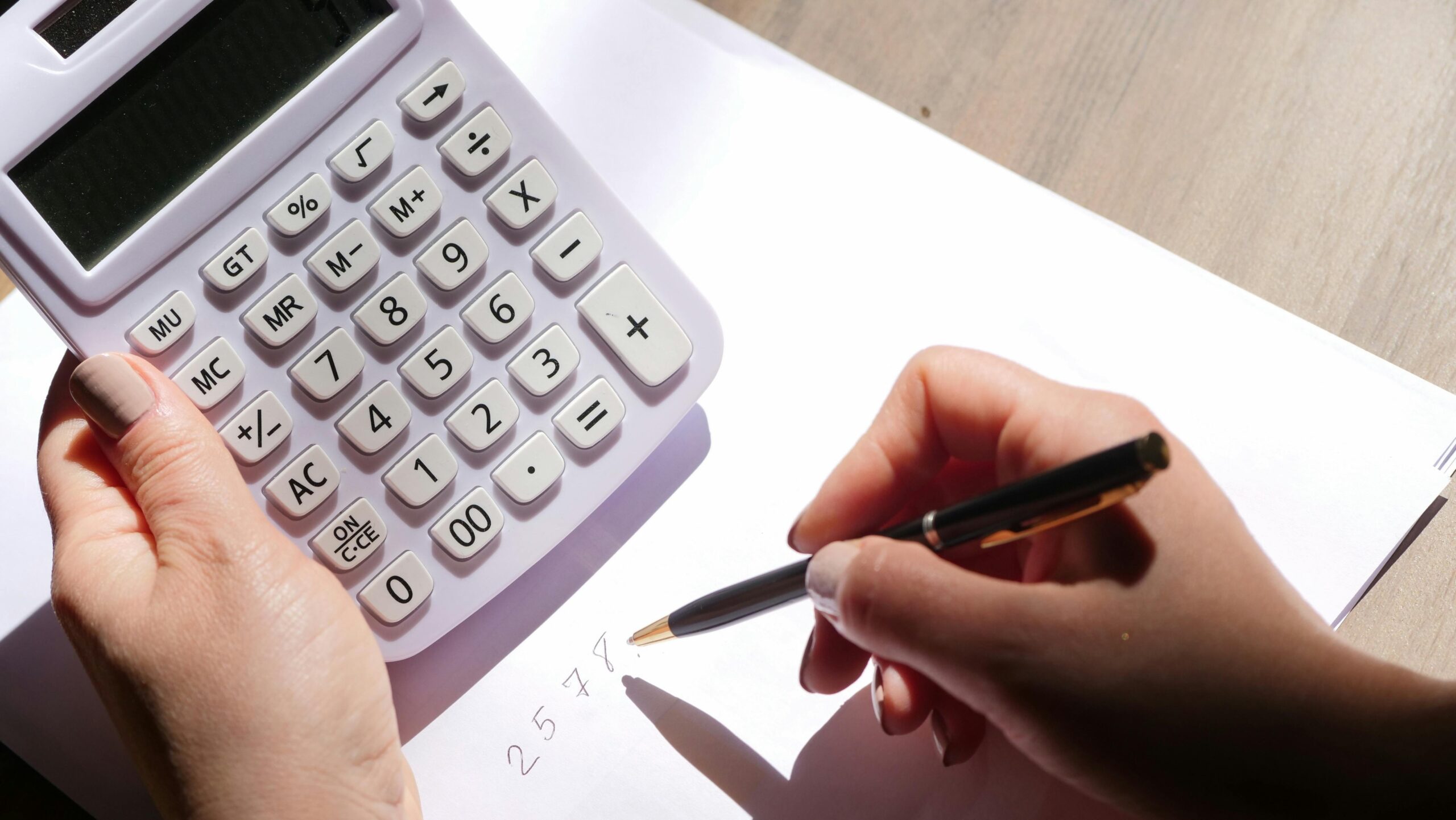 Hands holding a calculator and writing numbers, representing the detailed work of an outsourced accountant.