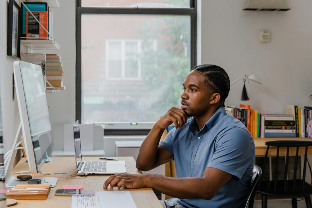 A focused professional reviewing data on a desktop and laptop, utilizing software for virtual assistants to manage projects.