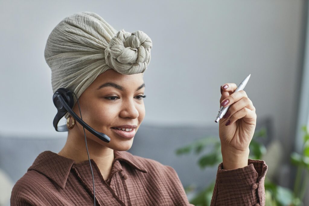 Virtual assistant in a headwrap, giving professional virtual assistant tips while holding a pen and wearing a headset.