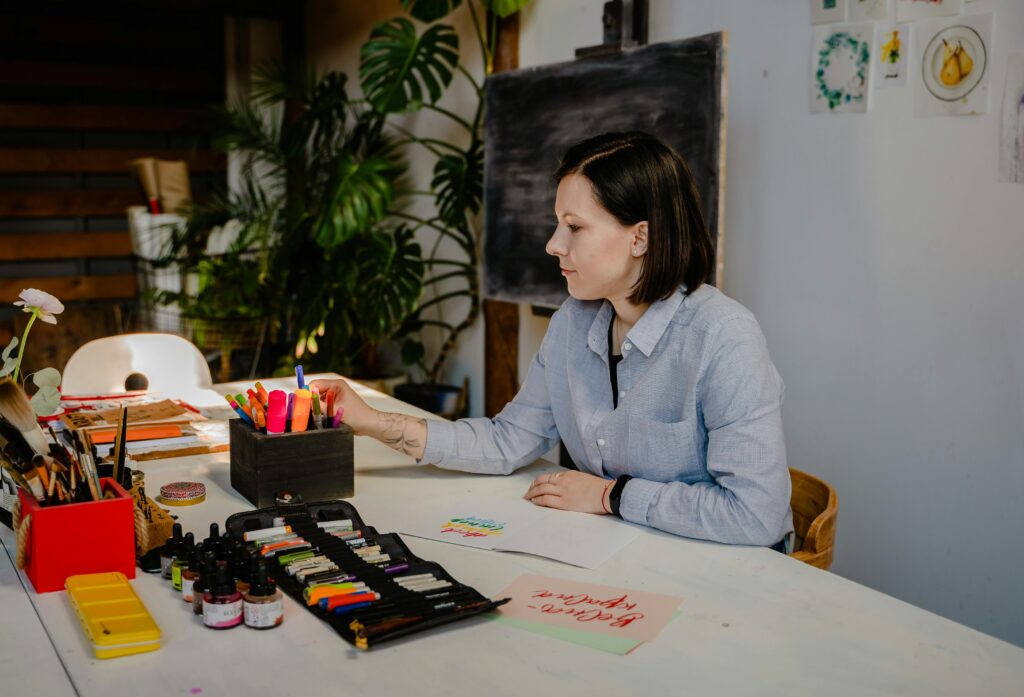 A professional organizing markers and art supplies at a creative workspace, demonstrating multitasking and resource management, critical skills for administrative assistants.