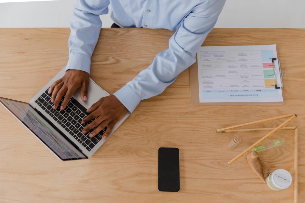 A professional reviewing documents and using a laptop, analyzing offshore outsourcing examples to improve business operations.