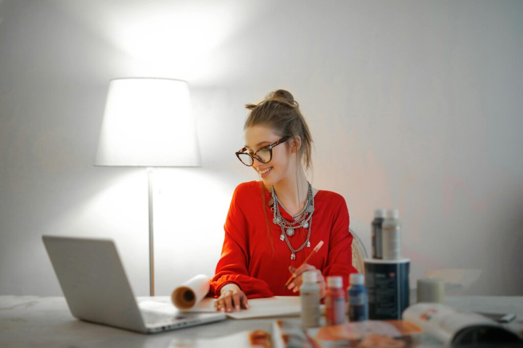 A creative professional in a vibrant red blouse working on a laptop, illustrating the creative and organizational benefits of why hire a virtual assistant.