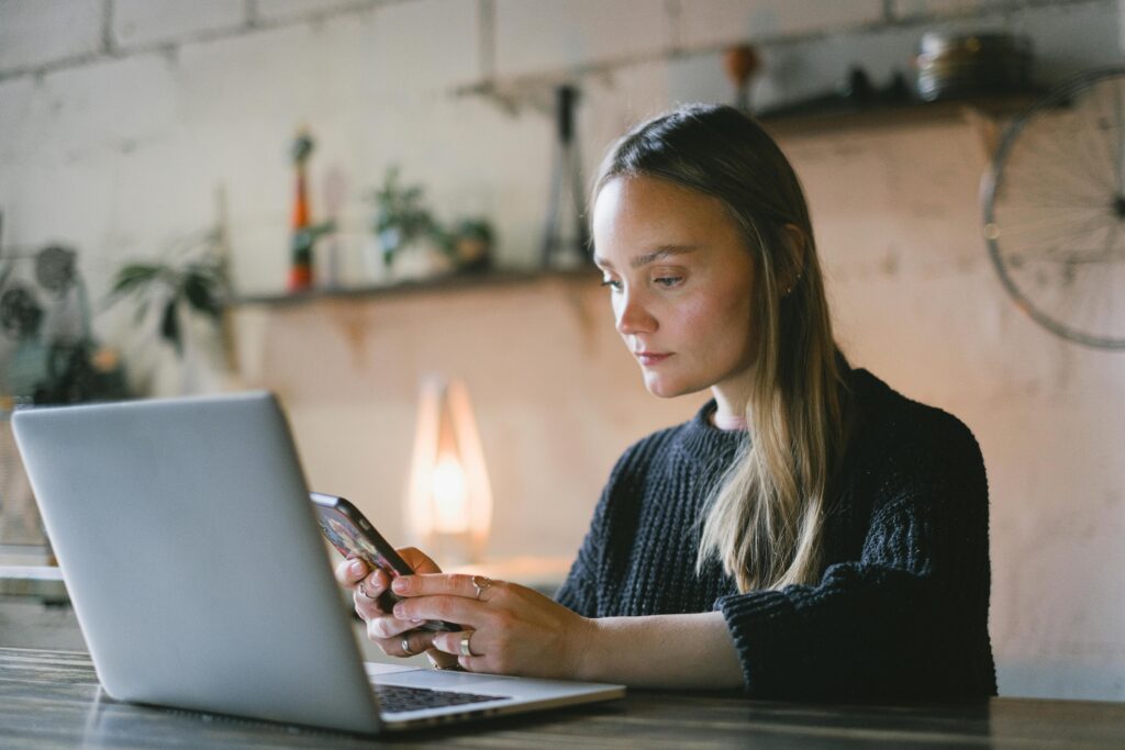 A focused woman using her phone and laptop simultaneously, illustrating the versatility of a virtual assistant for healthcare tasks.