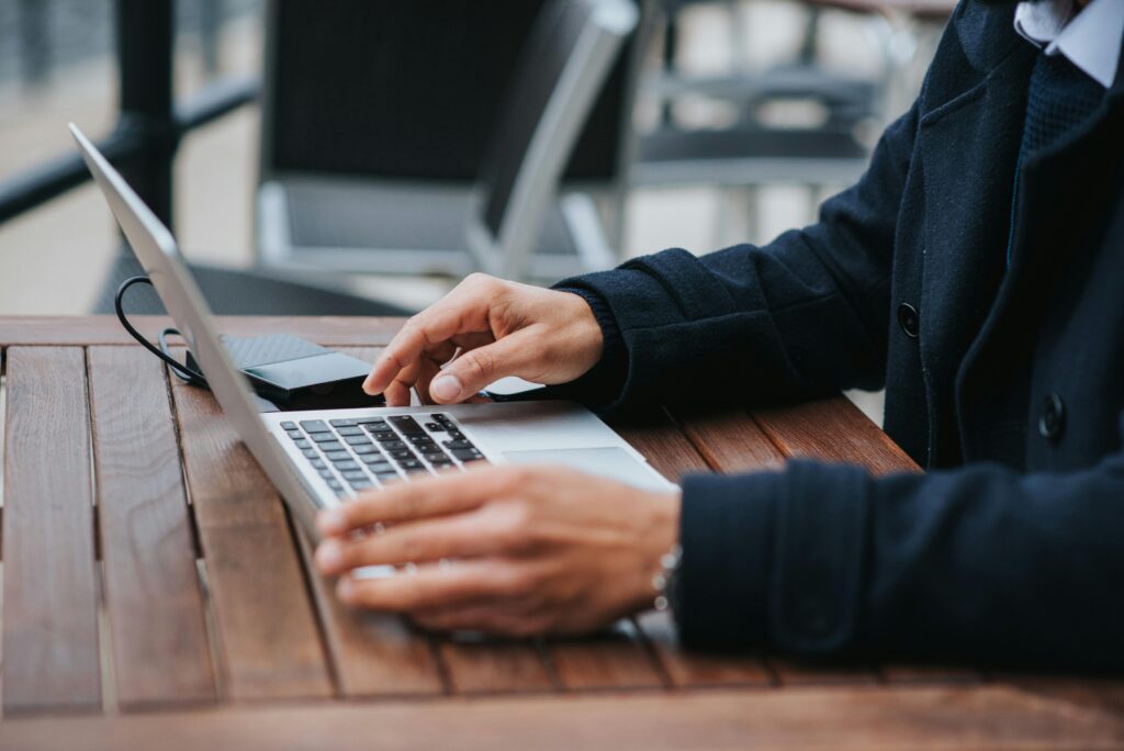 A marketing automation specialist working on a laptop at an outdoor table, with an external hard drive connected to the laptop.