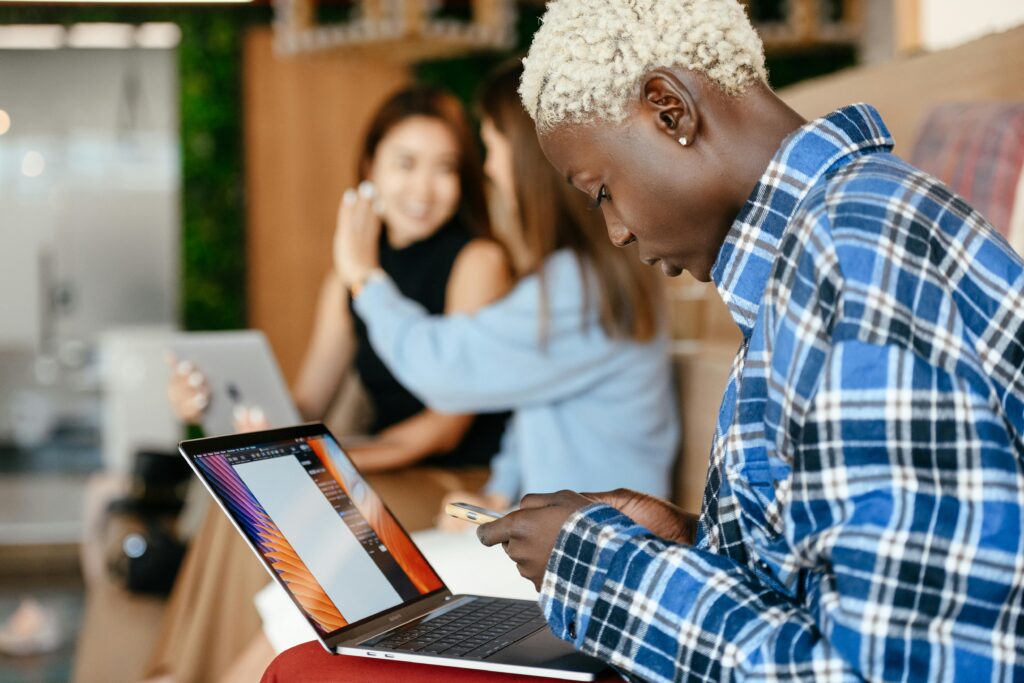A focused individual working on a laptop while multitasking on their smartphone, illustrating the multitasking capabilities of an Amazon virtual assistant.