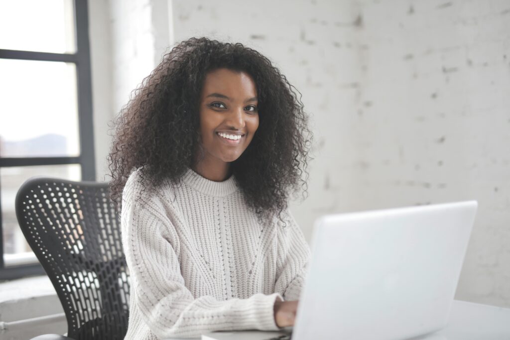 A smiling professional virtual assistant for eCommerce working on a laptop in a bright office setting.