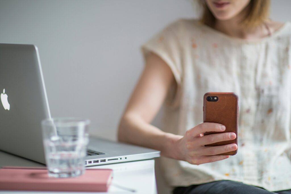 A focused individual using a smartphone while working on a laptop, highlighting the versatility of virtual admin assistant services for remote work management.