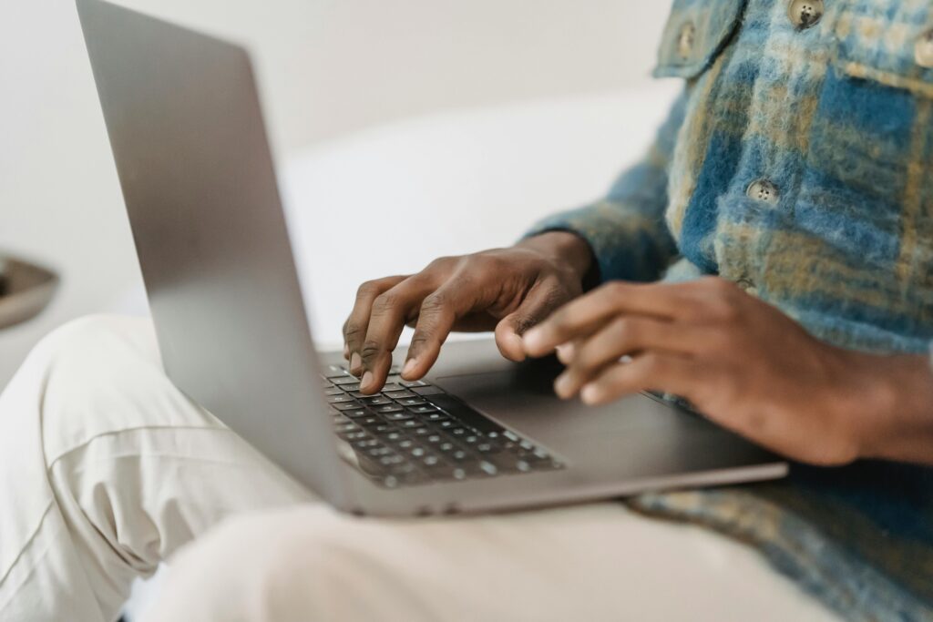 A marketing assistant typing on a laptop while wearing a blue and green plaid shirt.