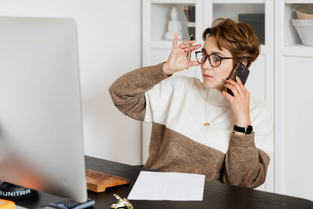 Professional wearing glasses and a color-block sweater engaged in a work call while reviewing documents, demonstrating key community management communication skills.