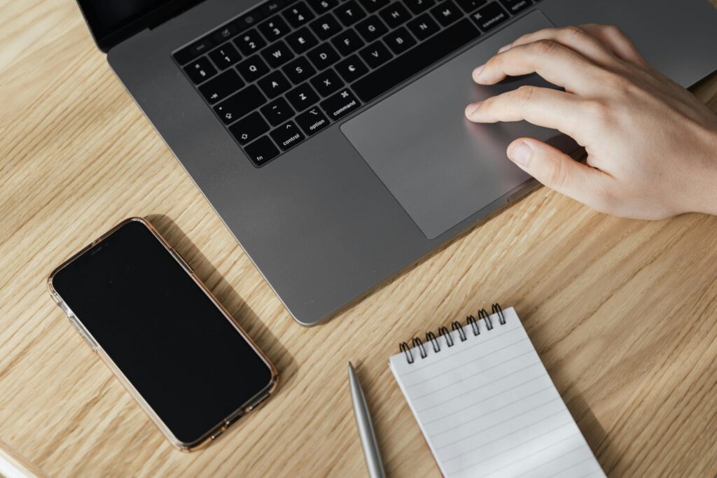 A workspace setup featuring a laptop, smartphone, notepad, and pen, highlighting the essential tools for an Amazon PPC manager key skills summary.