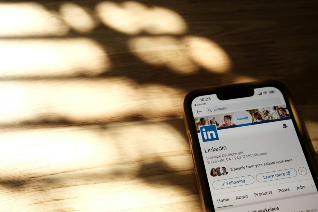 LinkedIn Ads expert key skills summary: Smartphone displaying a LinkedIn profile page on a wooden surface with sunlight casting shadows.