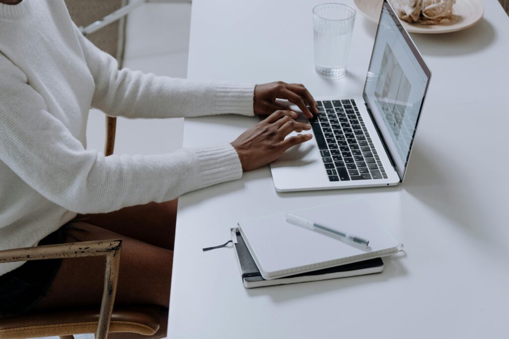 A focused workspace with a laptop displaying an Amazon PPC Manager Resume Template, accompanied by a notebook, pen, a glass of water, and a plate on a sleek white desk.