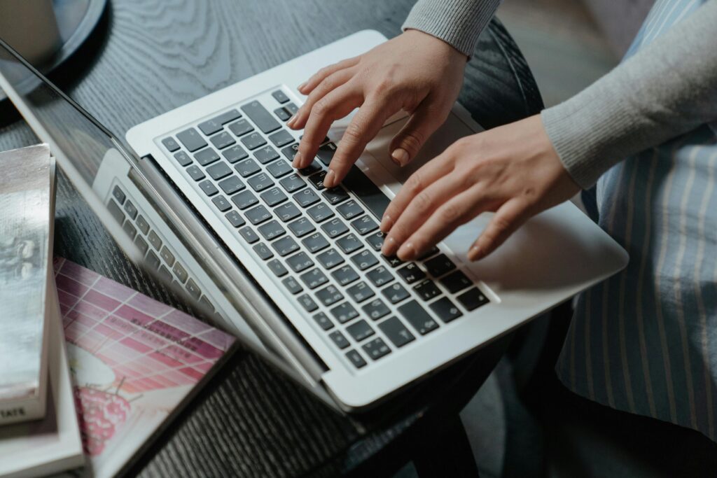 A person holding a white credit card while typing on a laptop keyboard, illustrating an E-commerce Marketing Manager Resume Template.