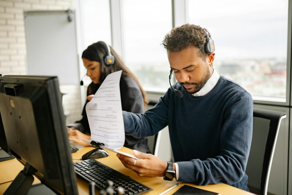 Two professionals wearing headsets work at their desks with computers and documents, illustrating an ideal environment for showcasing a CRM Manager Resume Template.