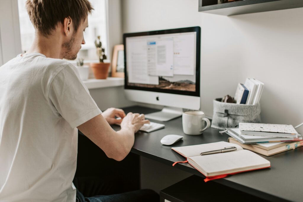 Man working on a desktop computer at a home office while editing an Email Marketing Specialist Resume Template.