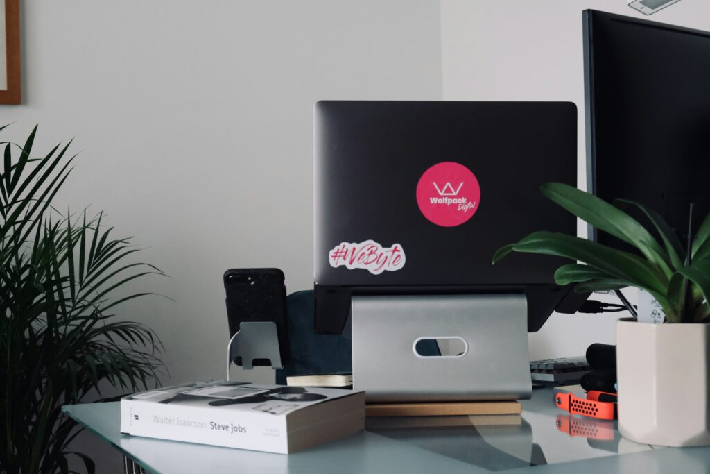 A high-angle view of a laptop displaying a variety of colorful website or app interface designs, with a coffee mug next to it on a wooden surface. The laptop screen also contains the text "Best Temp Agencies to Work With in 2025."