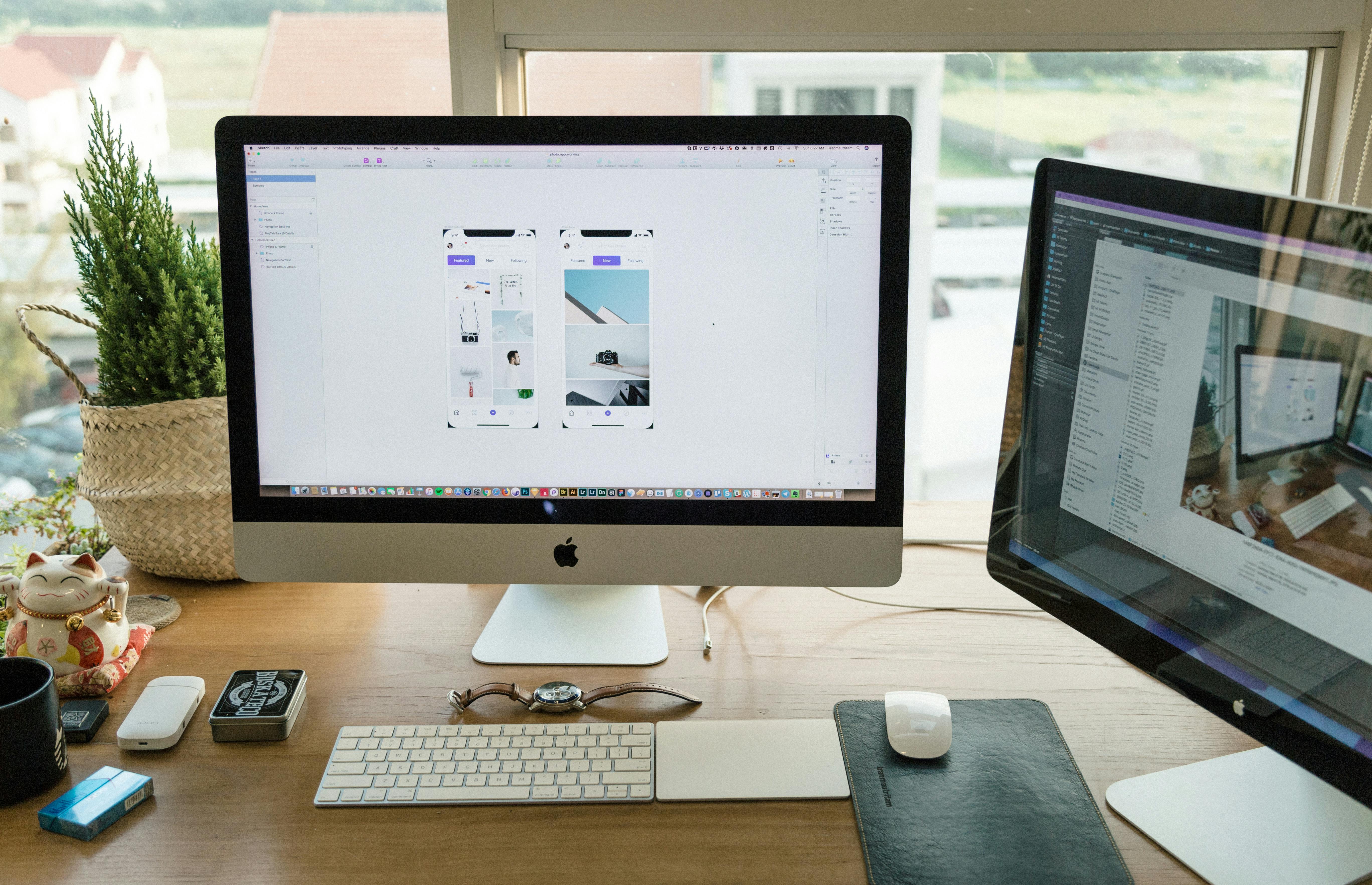 Modern workspace with dual monitors, design tools, and desk accessories near a window.