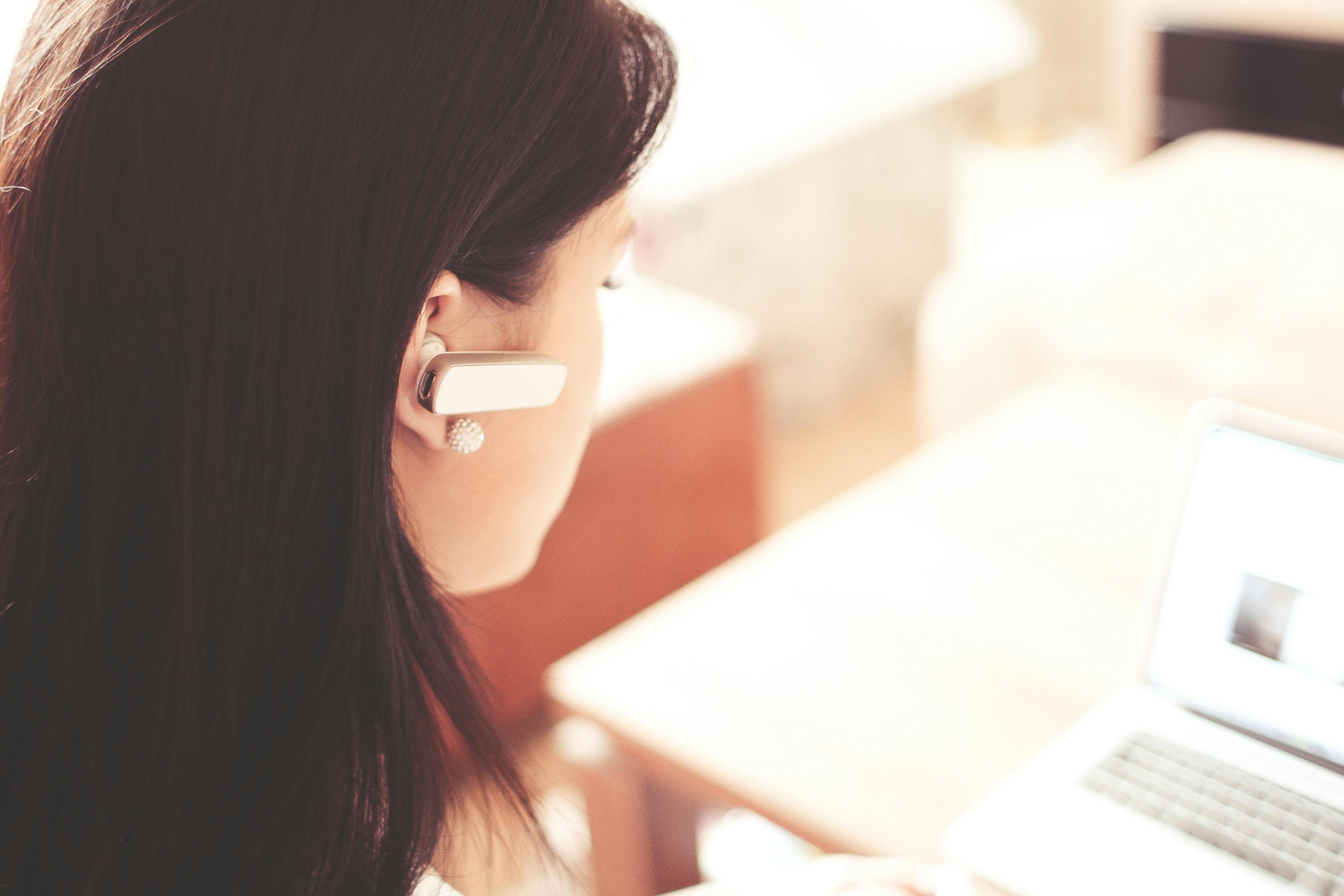 A close-up of a person wearing a Bluetooth earpiece, looking towards a laptop screen, suggesting active communication and review. This image reflects the in-depth analysis conducted when stating "I Reviewed the Top Customer Service Outsourcing Companies in 2025."