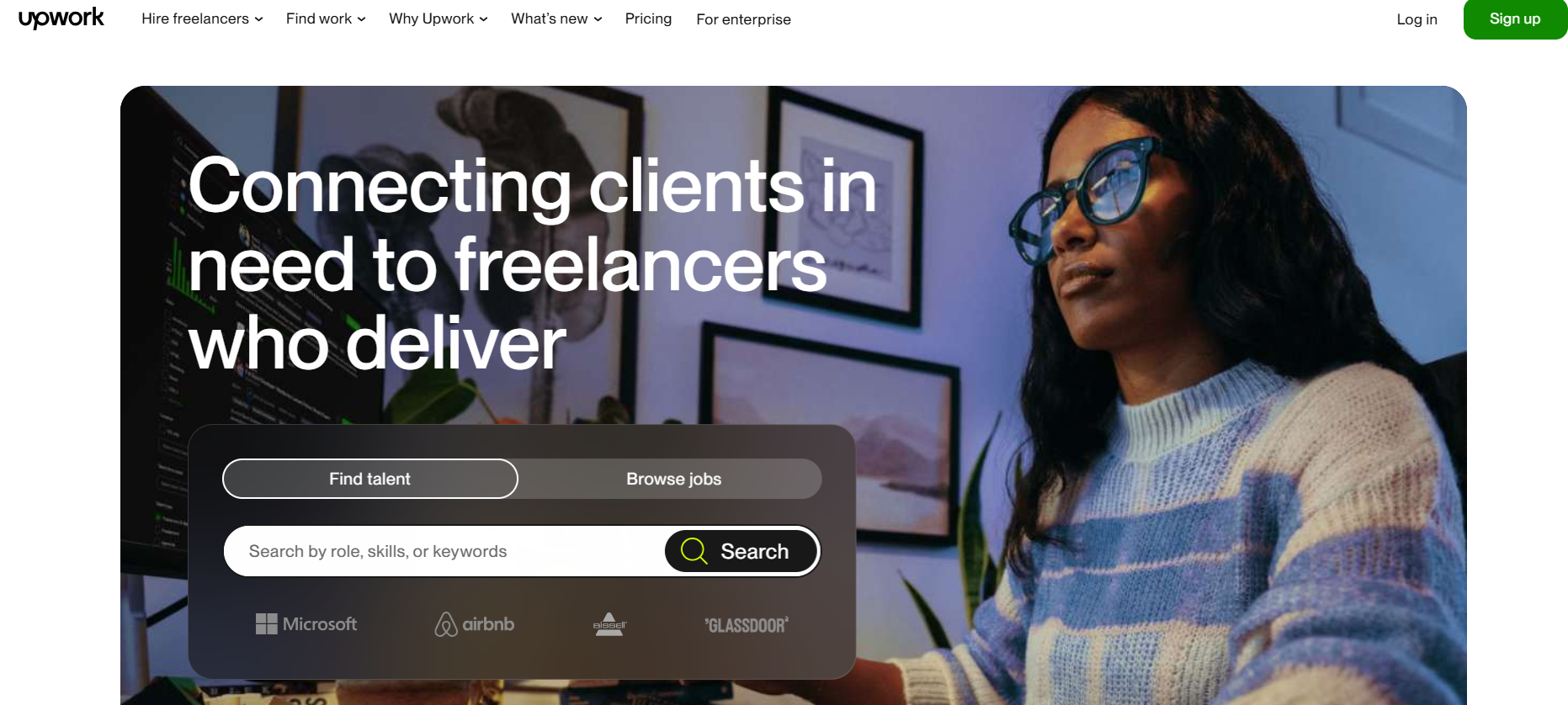 Screenshot of Upwork homepage featuring a woman in glasses and sweater working on a computer. Message "Connecting clients in need to freelancers who deliver," search bar with "Find talent" and "Browse jobs" tabs, logos of Microsoft, Airbnb, and Bissell, and top navigation with links to hiring, pricing, and enterprise solutions. Upwork branding included.