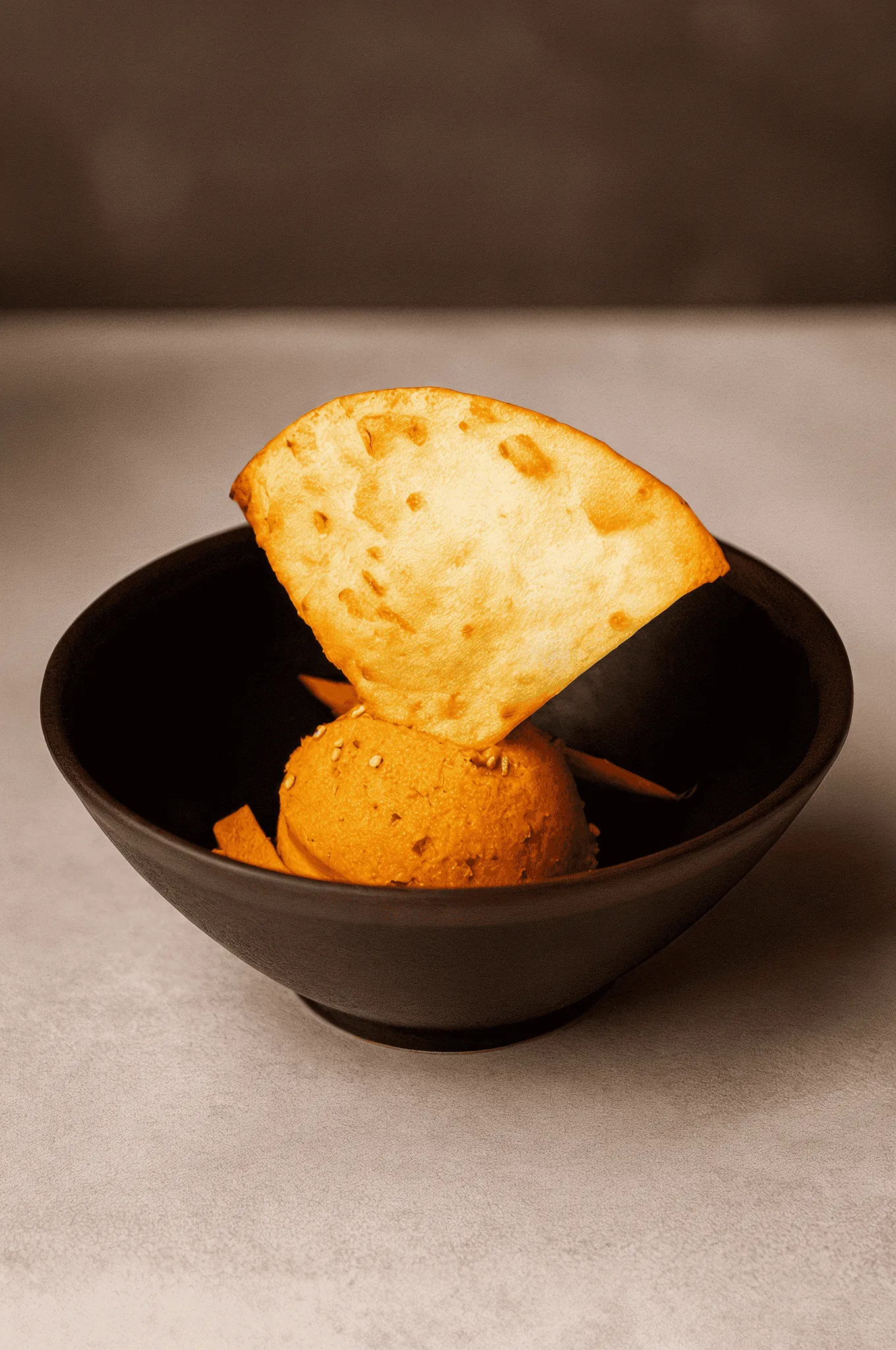 Golden tortilla chip with orange-colored ice cream in black bowl