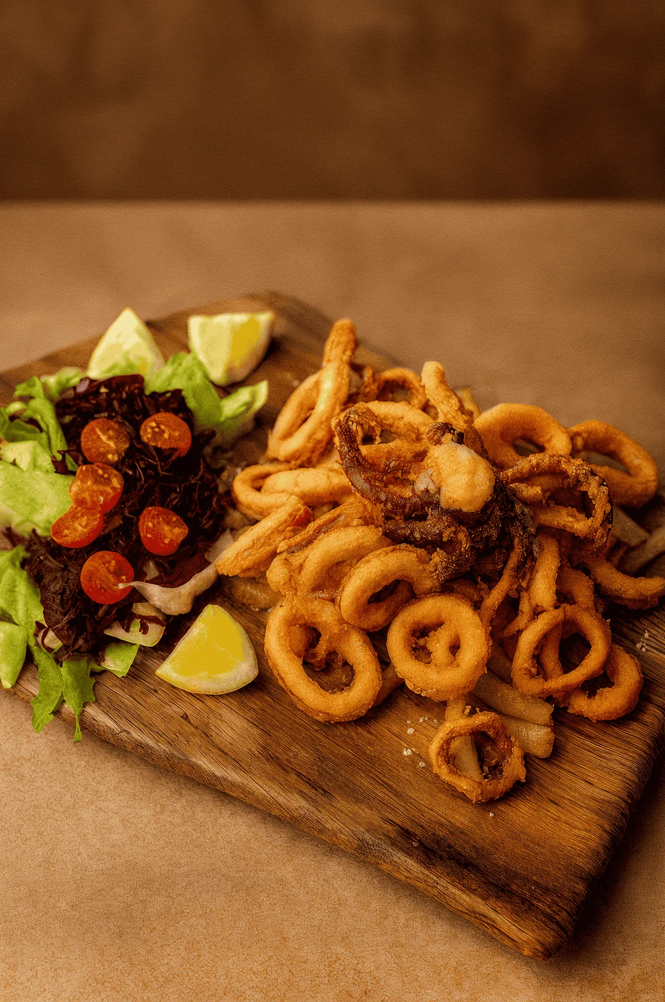 Crispy golden onion rings with salad and lemon wedges on wooden board
