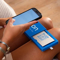 View of a Sleep Optimization Test box, opened and sitting on a woman's lap. The woman holds a smart phone over a QR code on the box to scan it. 