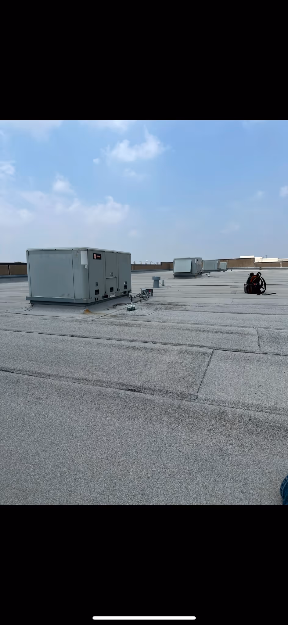 Air conditioning units are positioned on a flat rooftop under a clear sky.