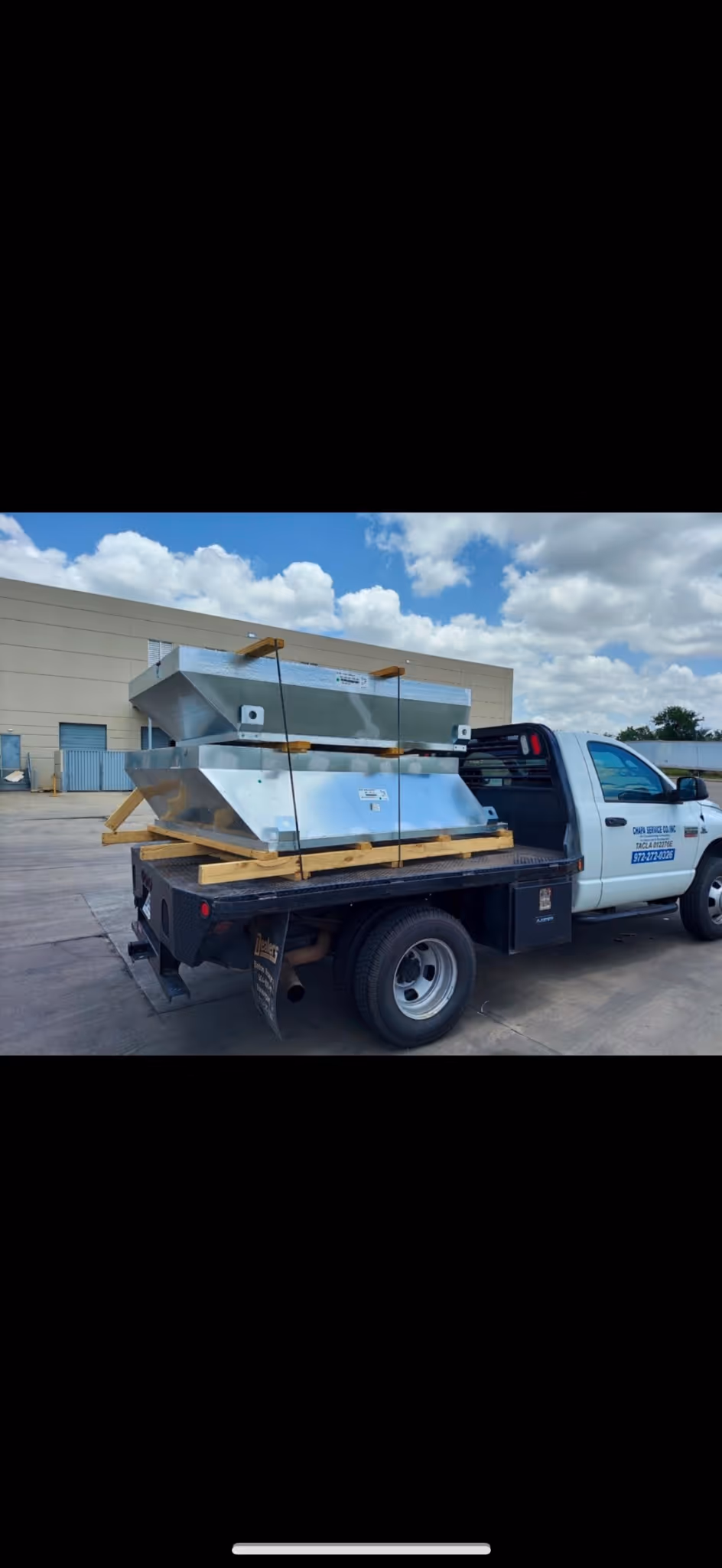 A white truck is parked, carrying large metallic equipment secured with straps on its flatbed.