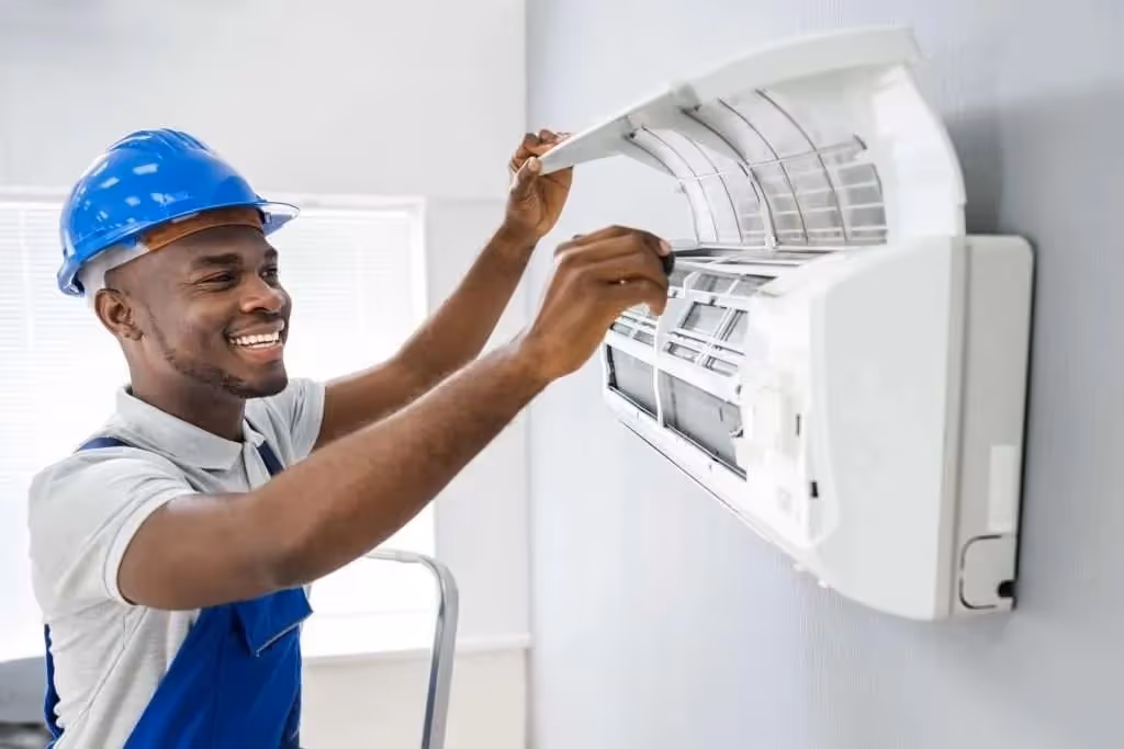 Smiling technician servicing wall-mounted AC unit.