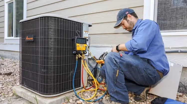 Technician servicing outdoor AC condenser unit with gauges.