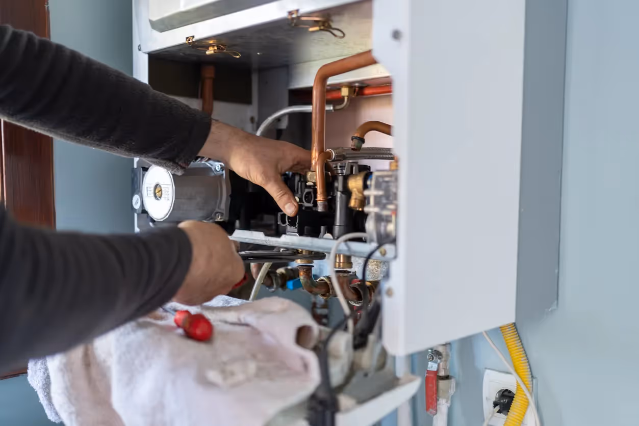 A close-up of a plumber's hands servicing the copper pipes and valves of a residential gas boiler.