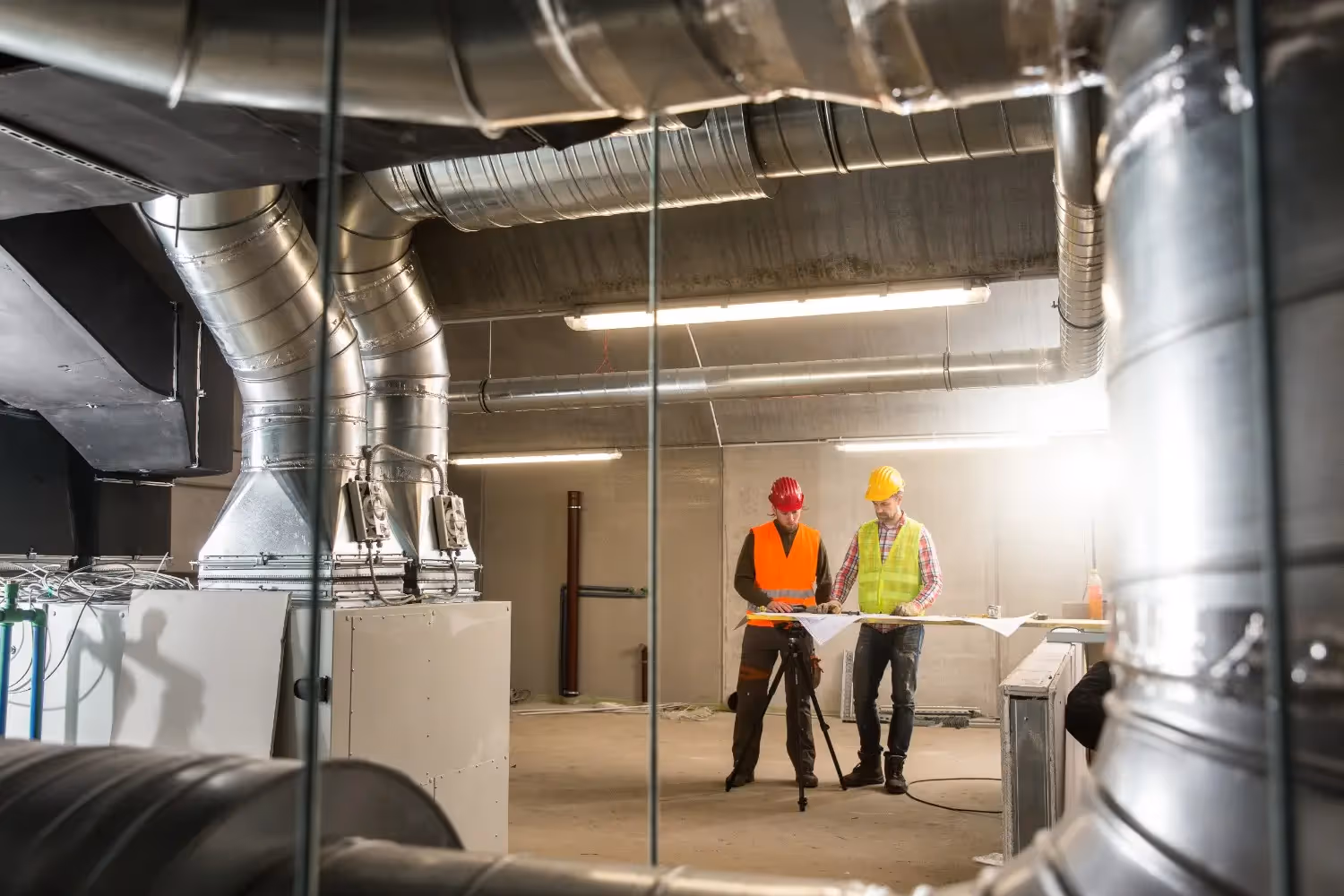 Workers review plans near HVAC ductwork.